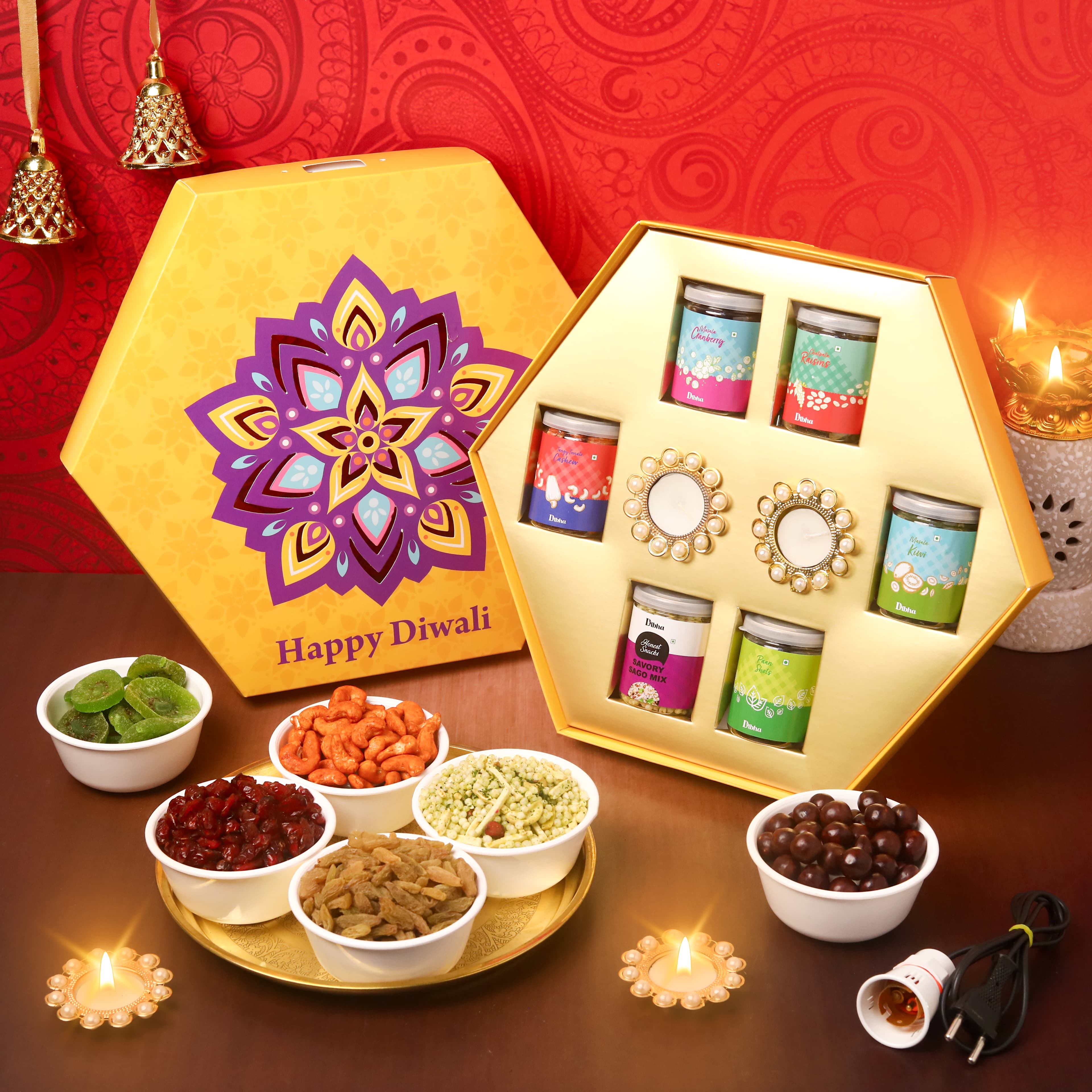 Yellow Diwali dry fruit gift box with assorted jars, bowls of snacks, diyas and red festive backdrop